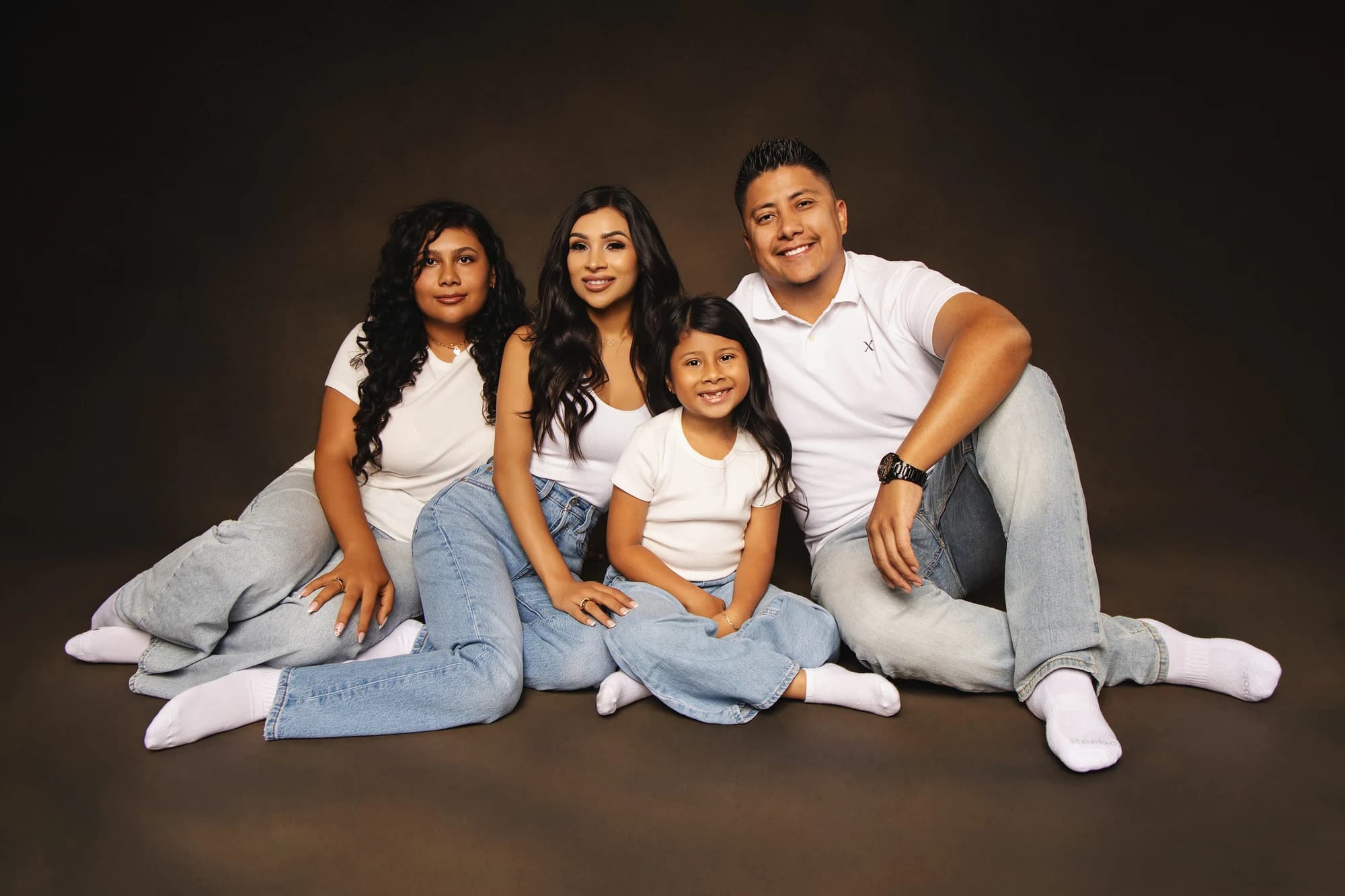 A family of four sitting together in white tops and blue jeans
