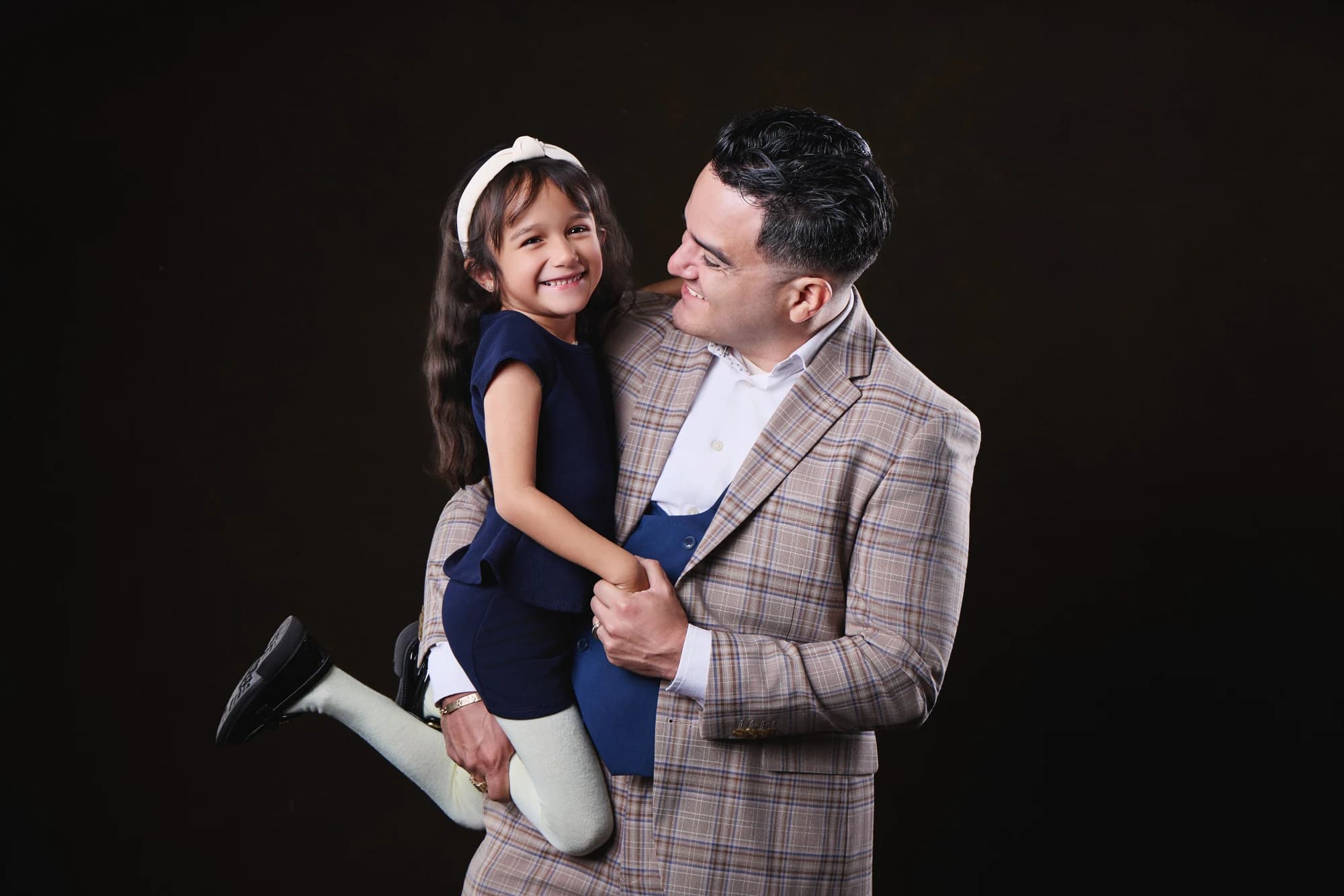 A father in a checked jacket holding his smiling daughter