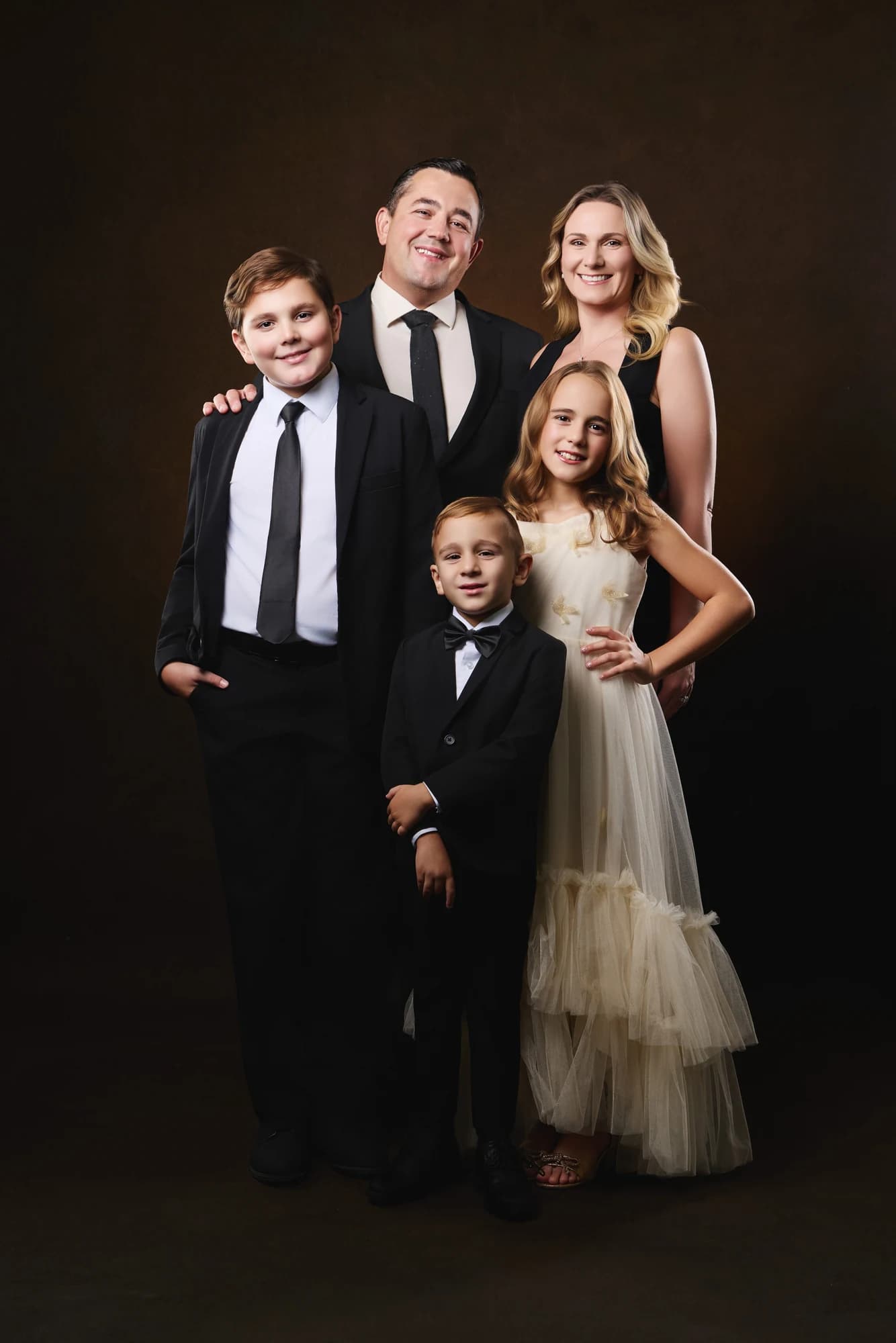 A family of five in formal clothing against a warm studio backdrop