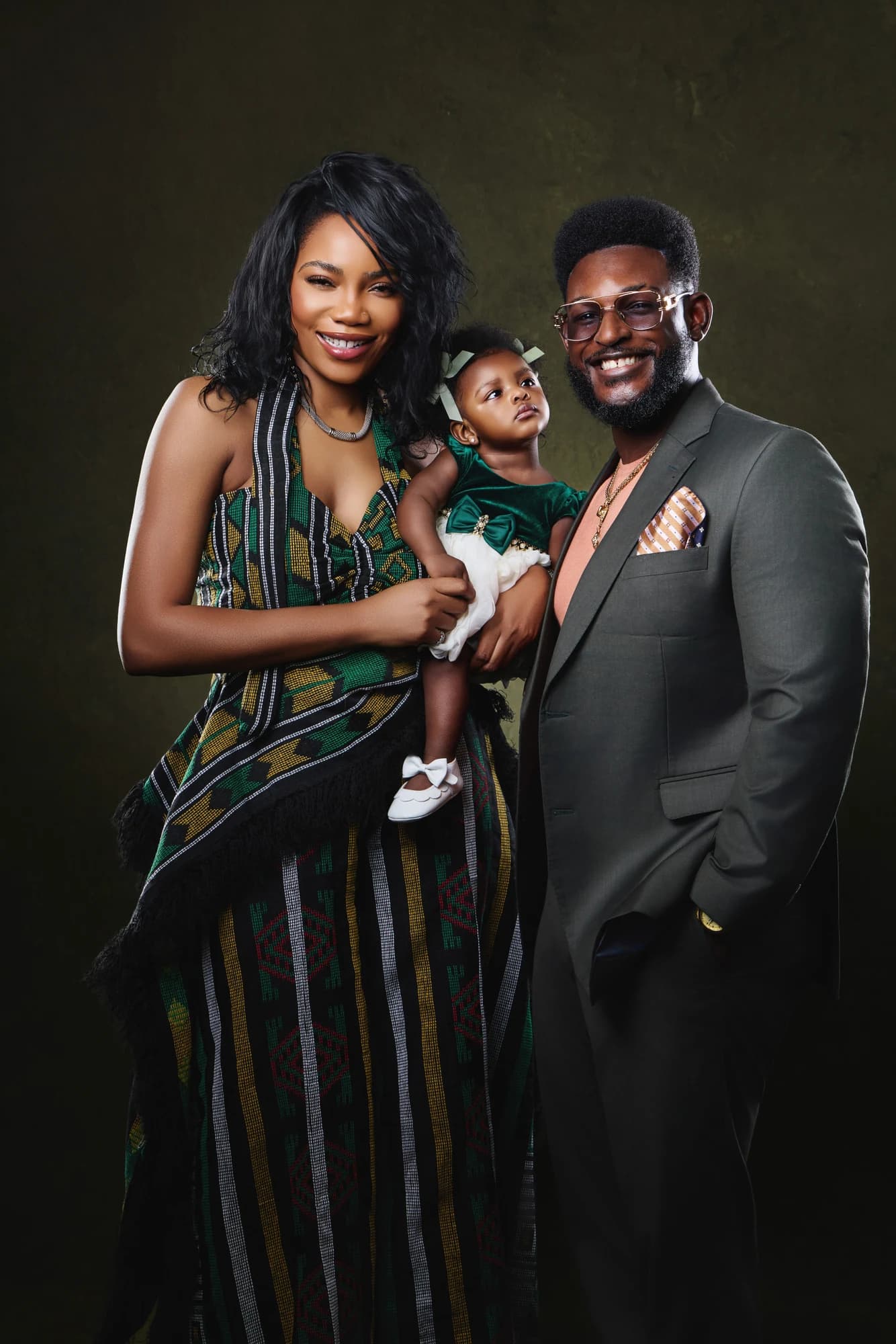 Parents holding their young daughter in a green and charcoal studio portrait