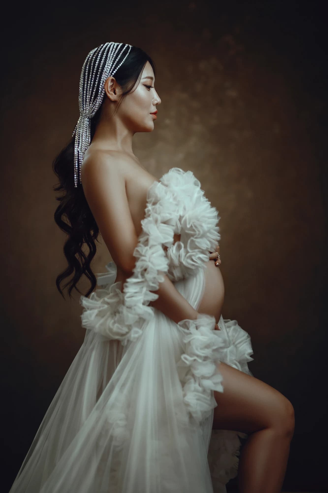 An expectant mother in profile holding ivory floral fabric against a warm backdrop