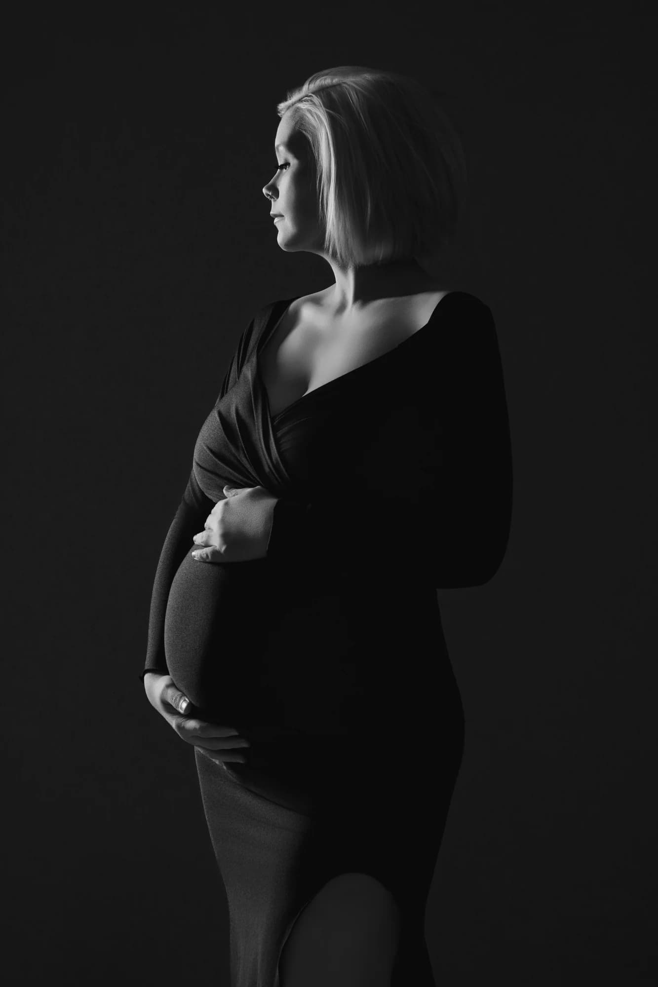 A black-and-white maternity portrait in a fitted black dress with soft side lighting