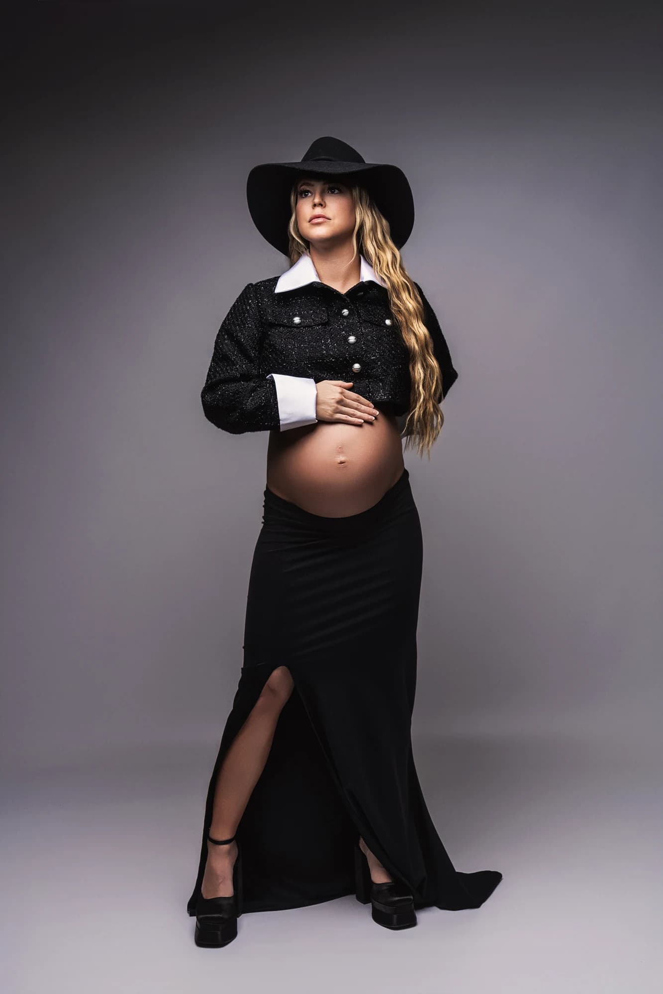 A western maternity portrait with a black hat, cropped jacket, and long skirt