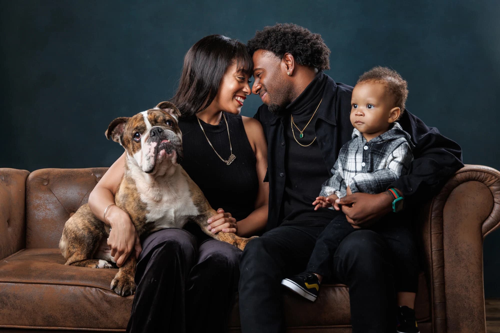 Parents and their young child together on a sofa with their brown-and-white dog