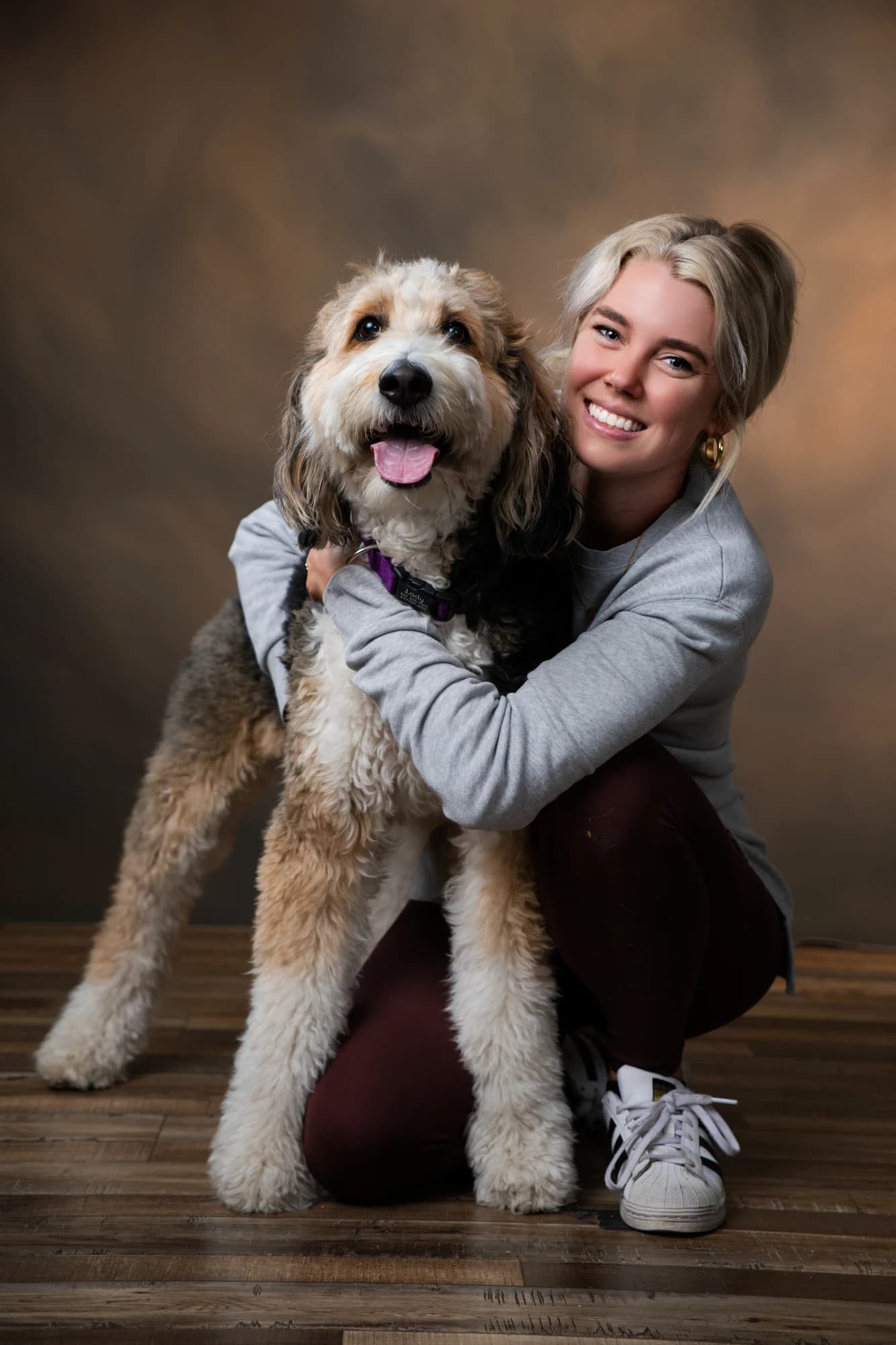 A smiling woman crouching to hug her shaggy dog