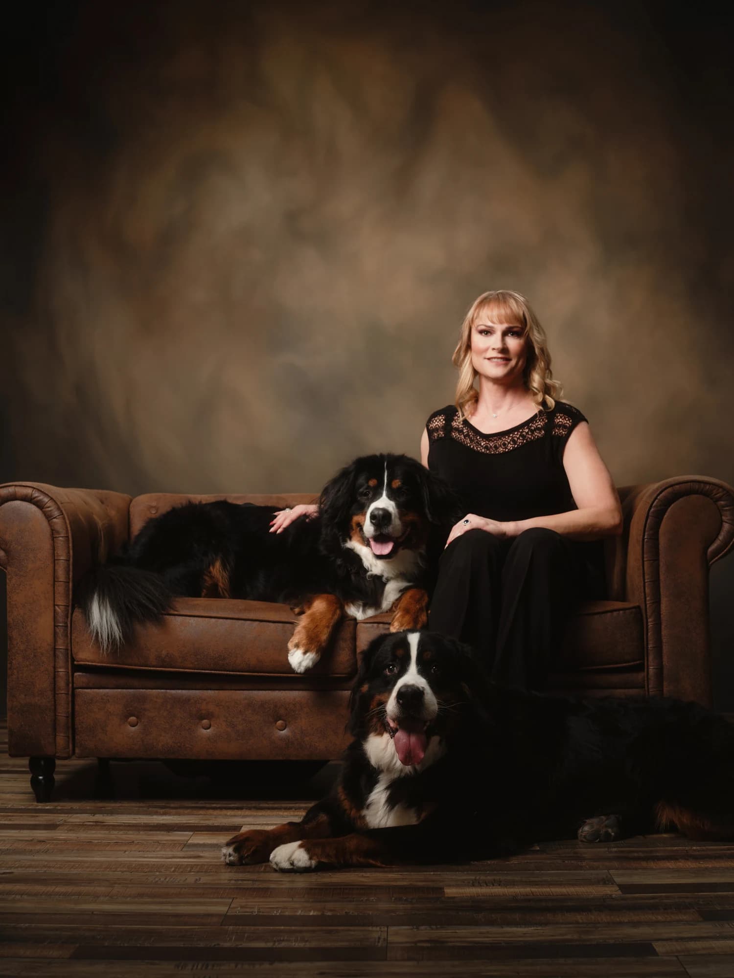 A woman seated on a leather sofa with two tricolor dogs